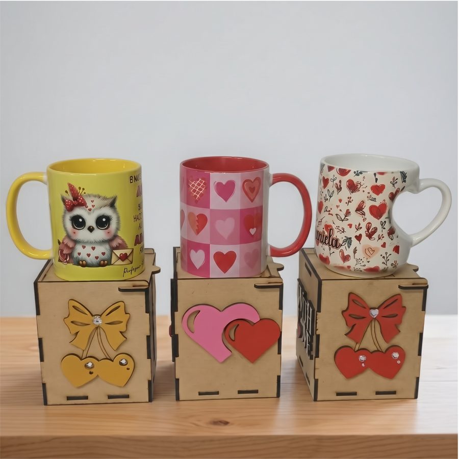 Tres tazas sublimadas con corazones y un búho, sobre cajas de MDF cortadas en láser con moños y corazones